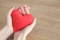 Hands of a young beautiful woman gently holding a red heart, on a wooden background, selective focus, save space. Royalty Free Stock Photo