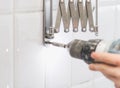 The hands of a young caucasian guy are tightening a screw on a metal fastener using a drill