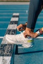 Hands of a young female runner tying the laces of her running shoes to jump an obstacle on a blue running track on a sunny day Royalty Free Stock Photo