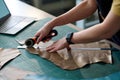 Hands of young female tailor cutting piece of beige leather