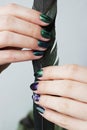 hands of a young girl with green manicure, which shows a sign of biological danger biohazard and black magpie feather. vertical.