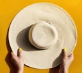 Hands of young girl holding straw hat on vibrant yellow background. Top View. Summer Travel Vacation Concept. Royalty Free Stock Photo