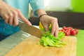 Hands of a young girl slice green lettuce leaves on a wooden cutting board on a green table in a home setting against a