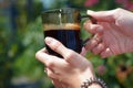 Hands of a young woman holding a cup of coffe in the garden lit by sunlight. Royalty Free Stock Photo