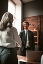 Handshake of business partners in office. Elderly woman and personable man stand at table shaking hands each other Royalty Free Stock Photo