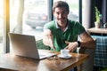 Handshake. Young happy businessman in green t-shirt sitting with laptop, toothy smile looking at camera and giving hand to Royalty Free Stock Photo