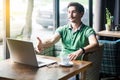 Handshake. Young satisfied businessman in green t-shirt sitting, looking at laptop screen, giving hand to greeting on interview