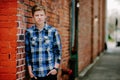 A handsom young man leans against a brick wall in an alley.