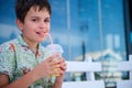 Handsome adorable Hispanic teenage boy drinking healthy smoothie, looking at camera, sitting on a cafe outdoor