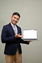 Handsome adult Asian businessman holding laptop mockup, open his palm at the screen Royalty Free Stock Photo