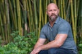 Handsome adult male model with a beard and bald head posing in a bamboo garden scene Royalty Free Stock Photo