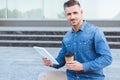 Handsome adult man with a coffee cup holding digital tablet, looking at camera and sitting