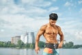 Sportsman with naked torso showing muscles near lake.
