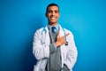 Handsome african american doctor man wearing coat and stethoscope over blue background cheerful with a smile on face pointing with Royalty Free Stock Photo