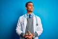 Handsome african american doctor man wearing coat and stethoscope over blue background doing money gesture with hands, asking for Royalty Free Stock Photo