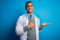 Handsome african american doctor man wearing coat and stethoscope over blue background Showing palm hand and doing ok gesture with Royalty Free Stock Photo