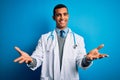 Handsome african american doctor man wearing coat and stethoscope over blue background smiling cheerful offering hands giving Royalty Free Stock Photo