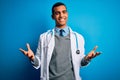 Handsome african american doctor man wearing coat and stethoscope over blue background smiling cheerful with open arms as friendly Royalty Free Stock Photo