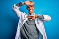 Handsome african american doctor man wearing coat and stethoscope over blue background Smiling cheerful playing peek a boo with Royalty Free Stock Photo