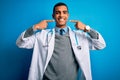 Handsome african american doctor man wearing coat and stethoscope over blue background smiling cheerful showing and pointing with Royalty Free Stock Photo