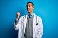 Handsome african american doctor man wearing coat and stethoscope over blue background smiling with happy face looking and Royalty Free Stock Photo