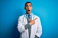 Handsome african american doctor man wearing coat and stethoscope over blue background Surprised pointing with finger to the side, Royalty Free Stock Photo