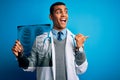 Handsome african american doctor man wearing stethoscope holding chest xray pointing and showing with thumb up to the side with Royalty Free Stock Photo