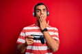 Handsome african american gamer man playing video game using jostick and headphones cover mouth with hand shocked with shame for Royalty Free Stock Photo