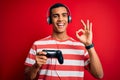 Handsome african american gamer man playing video game using jostick and headphones doing ok sign with fingers, excellent symbol Royalty Free Stock Photo