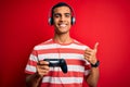 Handsome african american gamer man playing video game using jostick and headphones happy with big smile doing ok sign, thumb up Royalty Free Stock Photo