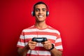 Handsome african american gamer man playing video game using jostick and headphones with a happy face standing and smiling with a Royalty Free Stock Photo