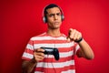 Handsome african american gamer man playing video game using jostick and headphones pointing with finger to the camera and to you, Royalty Free Stock Photo