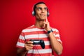 Handsome african american gamer man playing video game using jostick and headphones serious face thinking about question, very Royalty Free Stock Photo