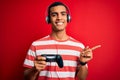 Handsome african american gamer man playing video game using jostick and headphones very happy pointing with hand and finger to Royalty Free Stock Photo