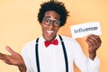 Handsome african american man with afro hair holding paper with influencer text celebrating achievement with happy smile and