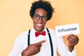 Handsome african american man with afro hair holding paper with influencer text smiling happy pointing with hand and finger