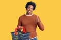 Handsome african american man with afro hair holding supermarket shopping basket smiling happy and positive, thumb up doing Royalty Free Stock Photo