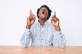 Handsome african american man with afro hair wearing casual clothes sitting on the table amazed and surprised looking up and Royalty Free Stock Photo