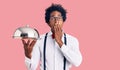 Handsome african american man with afro hair wearing waiter uniform holding silver tray covering mouth with hand, shocked and Royalty Free Stock Photo