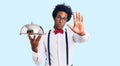 Handsome african american man with afro hair wearing waiter uniform holding silver tray with open hand doing stop sign with Royalty Free Stock Photo