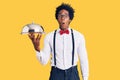 Handsome african american man with afro hair wearing waiter uniform holding silver tray scared and amazed with open mouth for Royalty Free Stock Photo