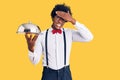 Handsome african american man with afro hair wearing waiter uniform holding silver tray stressed and frustrated with hand on head, Royalty Free Stock Photo