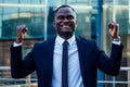 A handsome African American man in a black stylish suit and a white shirt rejoicing in success and thanking God against Royalty Free Stock Photo