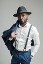 Handsome african american man in hat and suspenders holding jacket on shoulder with hand in pocket Royalty Free Stock Photo