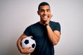 Handsome african american man playing footbal holding soccer ball over white background laughing and embarrassed giggle covering Royalty Free Stock Photo