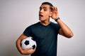 Handsome african american man playing footbal holding soccer ball over white background smiling with hand over ear listening an Royalty Free Stock Photo