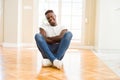 Handsome african american man sitting on the floor at home happy face smiling with crossed arms looking at the camera Royalty Free Stock Photo