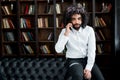 Handsome african american man sitting on sofa and talking on the phone in library Royalty Free Stock Photo