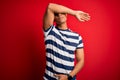 Handsome african american man wearing casual striped t-shirt standing over red background covering eyes with arm, looking serious Royalty Free Stock Photo