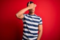 Handsome african american man wearing casual striped t-shirt standing over red background covering eyes with hand, looking serious Royalty Free Stock Photo